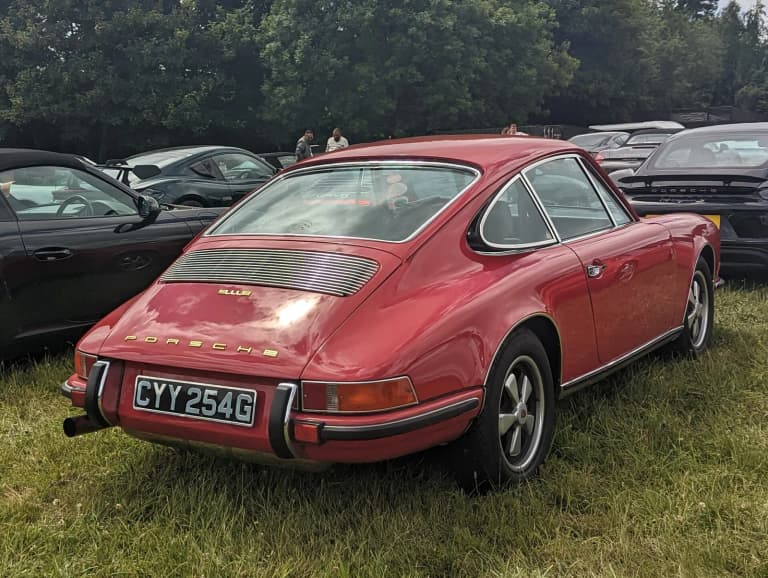 Red 1969 Porsche 911 E parked on grass at a classic car show.