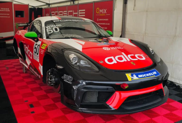 Porsche 718 GT4 race car in red and black livery in a paddock