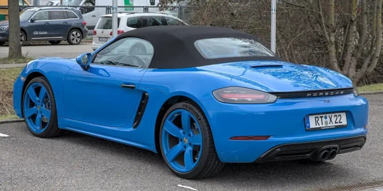 Blue Porsche 718 Boxster roadster with the soft top raised, rear three-quarter view