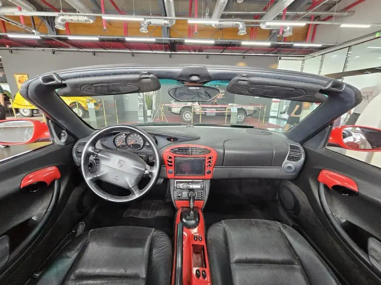 Porsche Boxster cabin with a three-spoke steering wheel, analog gauges, and red leather trim