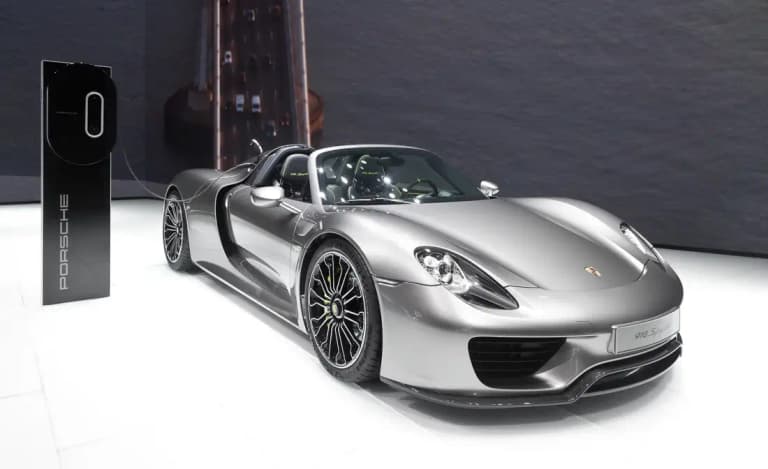 Silver Porsche 918 Spyder plugged into a charging pillar on a motor show stand