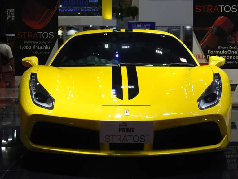 Yellow Ferrari 488 with black racing stripes on a display stand at a Thai motor show