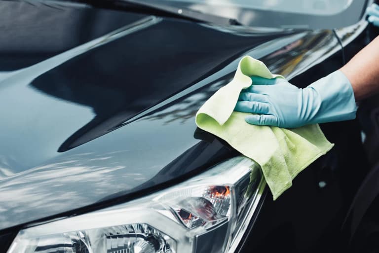 Detailer wiping a black car hood with a microfiber towel