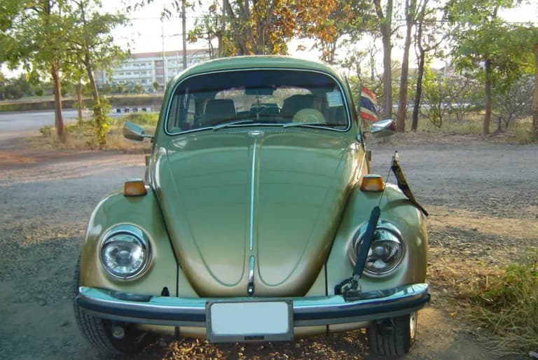 Green classic Volkswagen Beetle with a Thai flag parked in rural Thailand