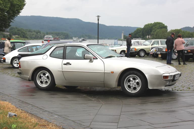 Silver Porsche 944 coupe in profile on a cobbled riverside