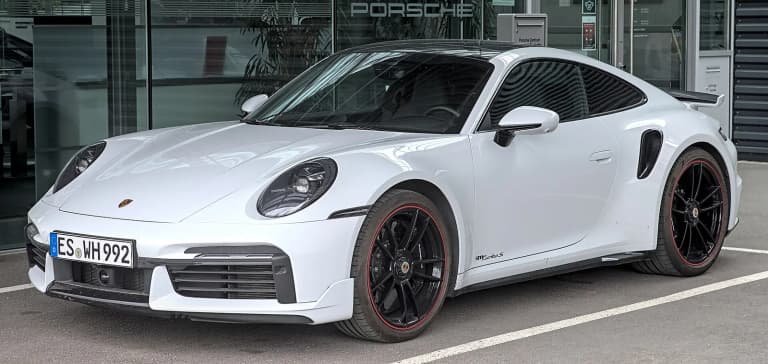 White Porsche 911 (992) Turbo S parked outside a Porsche dealership.