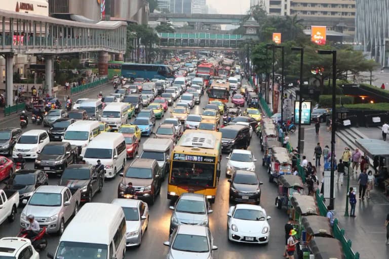 Dense Bangkok traffic with taxis, buses, tuk-tuks, and a white Porsche Cayman in the mix