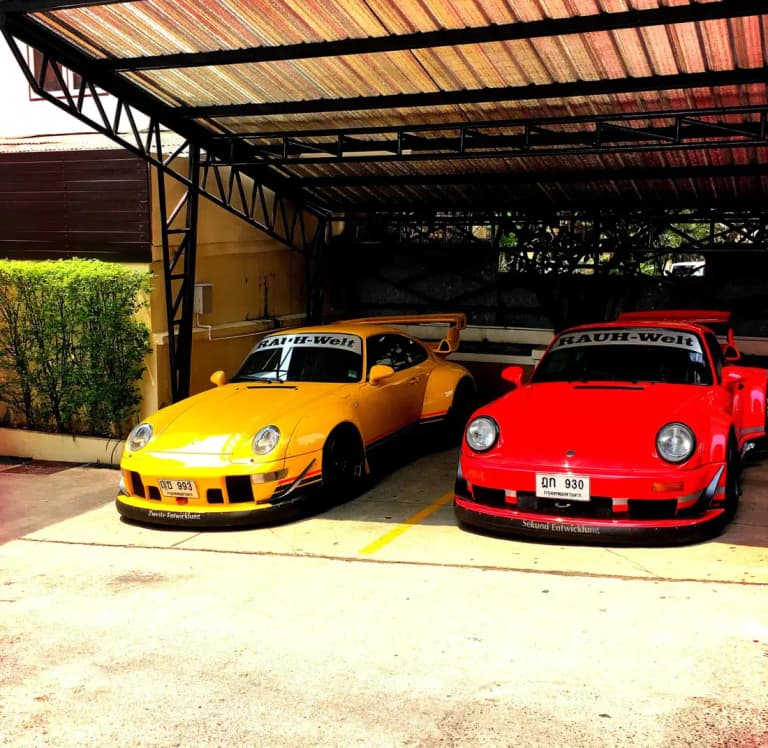 Yellow and red RWB widebody Porsche 911s with Bangkok license plates parked under a carport