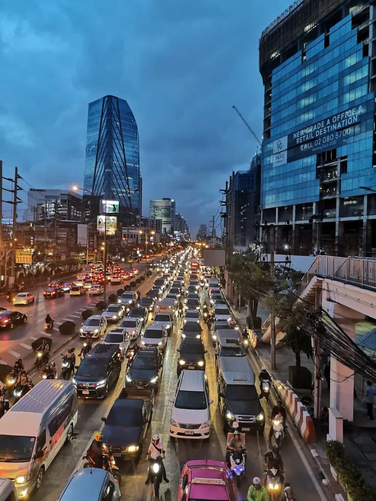 Evening traffic jam on a multi-lane Bangkok road with cars and motorcycles packed between skyscrapers