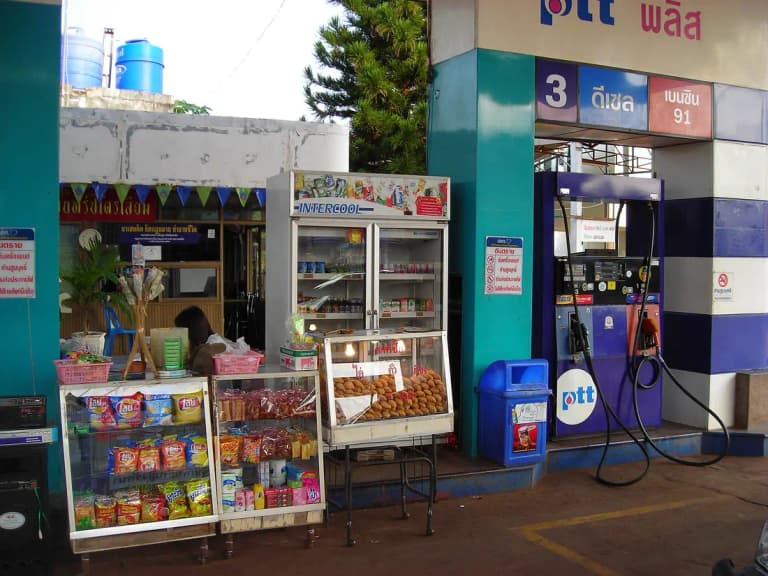 PTT gas station forecourt in Thailand with fuel pumps and a small roadside snack stall