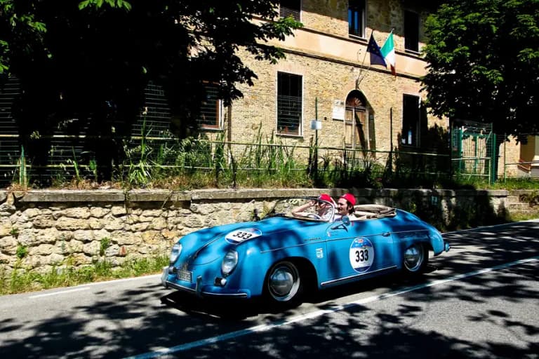 Blue Porsche 356 Speedster with low folding windscreen driving on a rural road