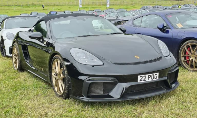 Black Porsche 718 Spyder with gold wheels parked in a field of Porsches