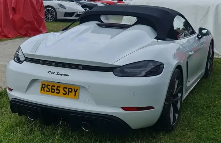 White Porsche 718 Spyder rear view showing the twin hump rear deck and black soft top