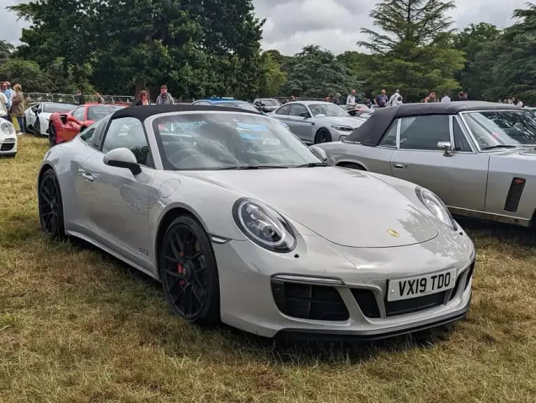 Silver Porsche 991 Targa 4 GTS with the Targa roll hoop and black wheels on grass