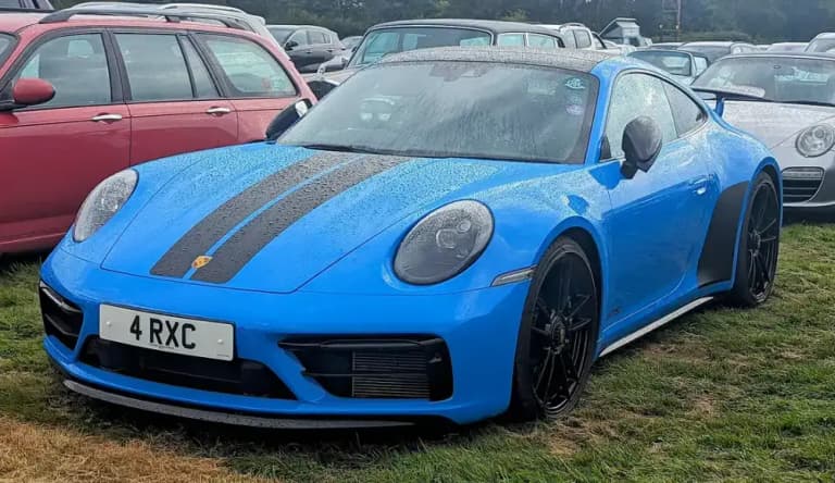 Blue Porsche 992 Carrera GTS coupe with black bonnet stripes and black wheels parked on grass