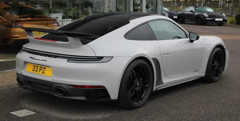 Rear three-quarter view of a white Porsche 992 Carrera GTS coupe showing the exhaust and 911 Carrera GTS script