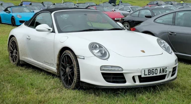 White Porsche 997 Carrera GTS Cabriolet with the roof up and black wheels parked on grass