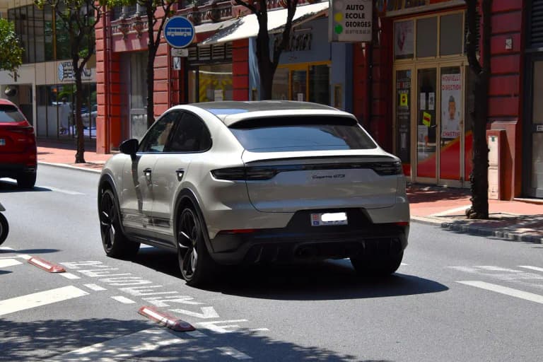 Chalk gray Porsche Cayenne GTS Coupe, rear three-quarter view showing the fastback roofline and rear spoiler
