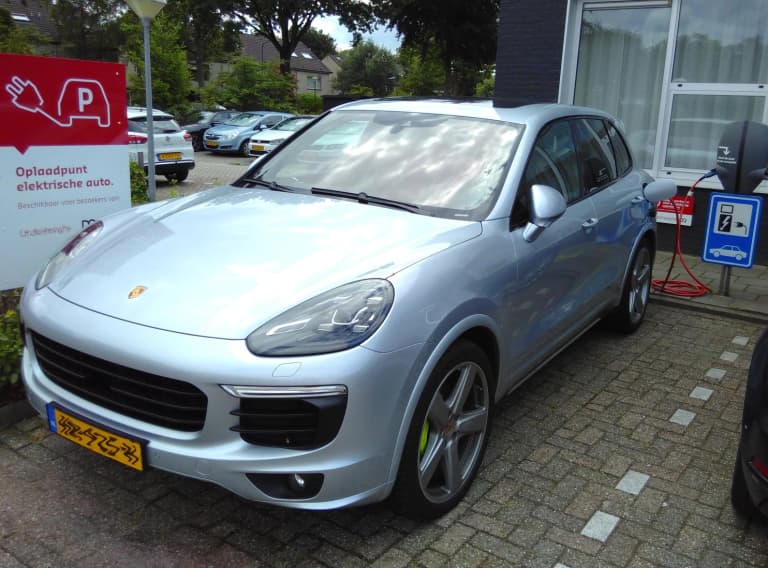 Silver Porsche Cayenne S E-Hybrid plugged into a public charging point, with green hybrid brake calipers