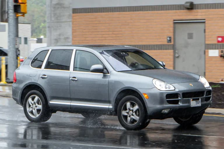Gray first-generation Porsche Cayenne S (955), front three-quarter view on a wet street