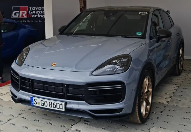 Light blue-gray Porsche Cayenne Turbo GT on a display stand, front three-quarter view