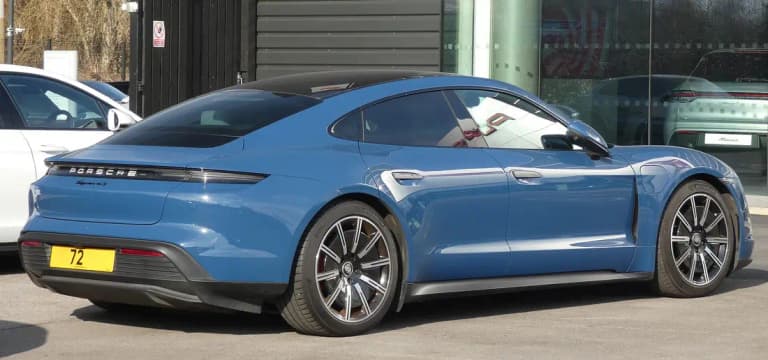 Blue Porsche Taycan 4S rear three-quarter view outside a Porsche dealer