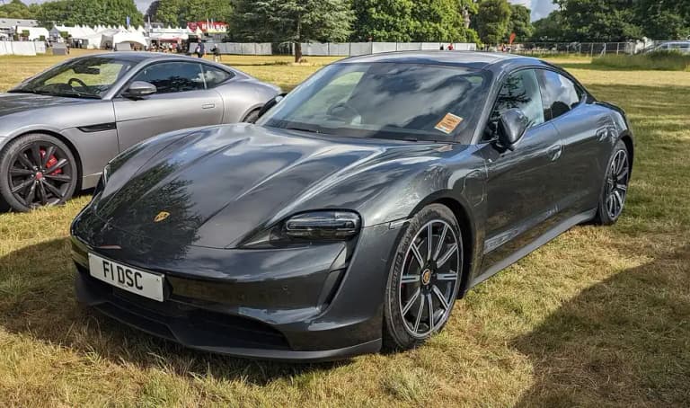 Dark grey Porsche Taycan 4S front three-quarter view on grass at a show