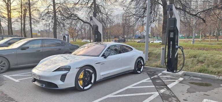 Grey Porsche Taycan plugged into a Porsche-branded DC fast charging pedestal