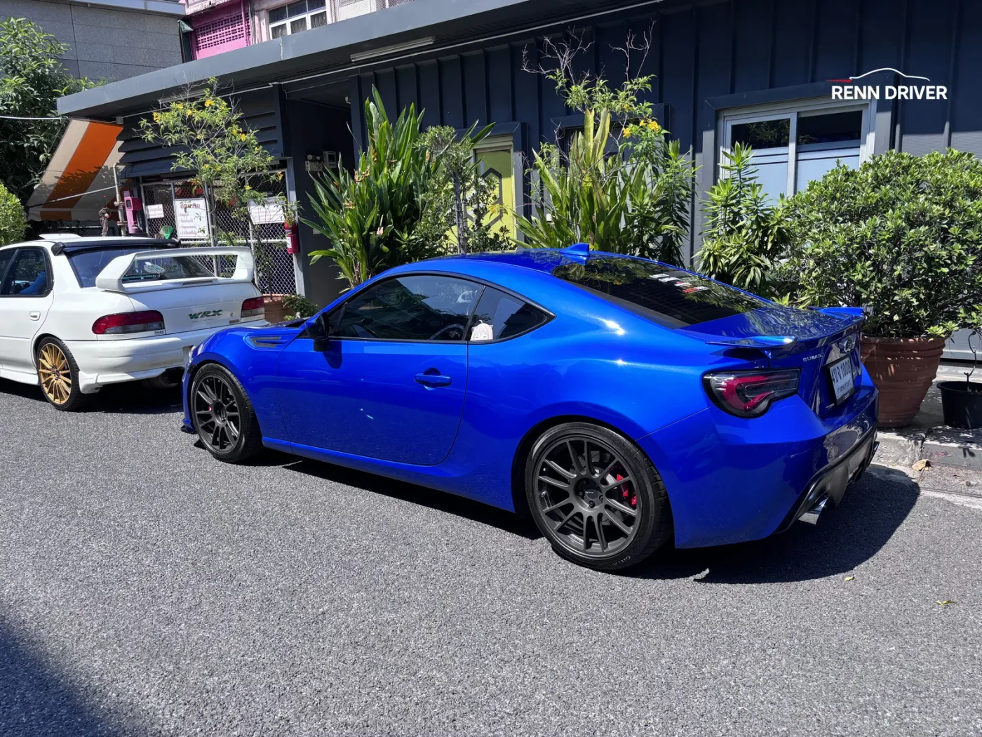Blue Toyota 86 coupe parked next to a white Subaru Impreza by a dark container unit