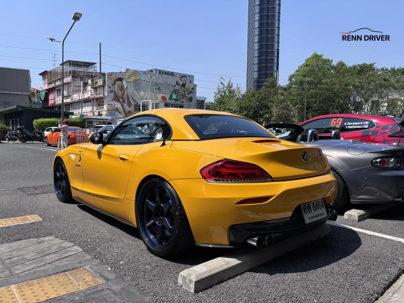 Yellow BMW Z4 parked at a car meet with a city tower in the background