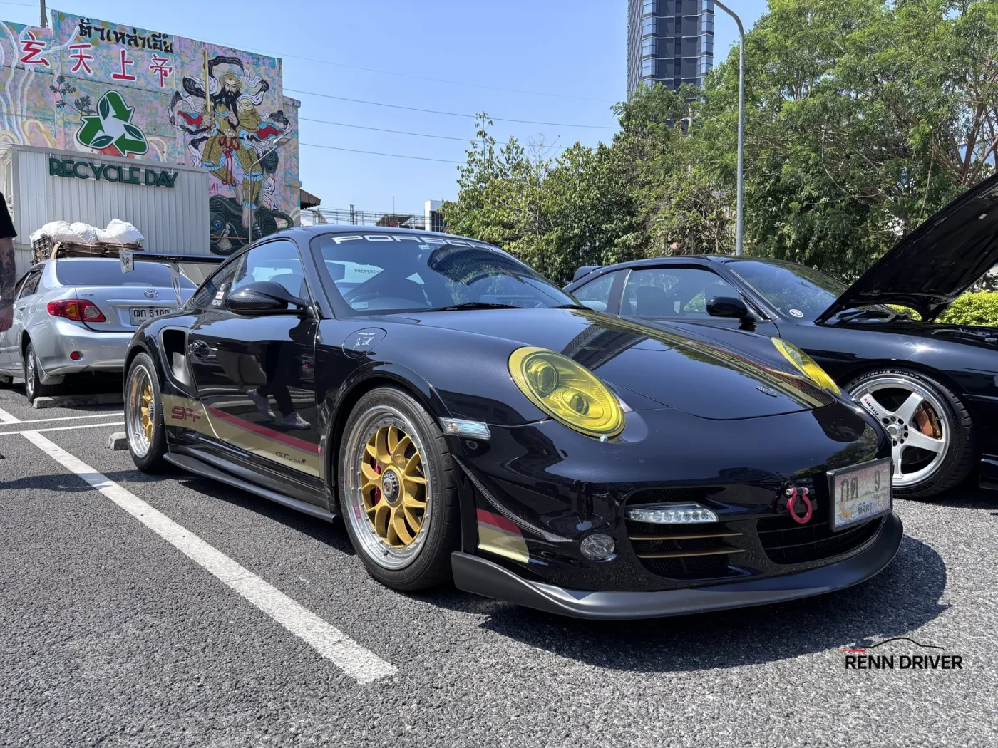 Black Porsche 997 Turbo on gold wheels with yellow headlights at a car meet